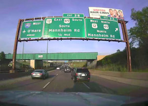 On-vehicle camera shows an overhead highway sign with exit information