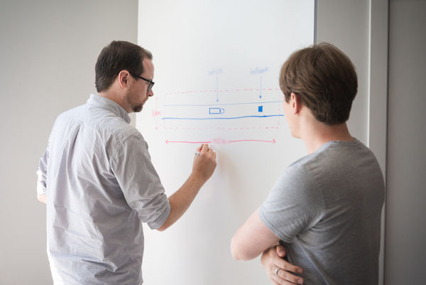 Two men looking at a diagram on a whiteboard.